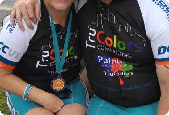 Two individuals wearing matching black athletic jerseys with a colorful "TruColors Contracting" logo, one displaying a medal around their neck.