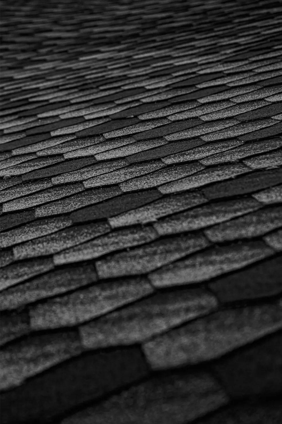 Close-up of a textured, dark gray roof with overlapping, class four shingles creating a pattern across the surface. These impact-resistant roofing shingles appear uniform in size and shape.